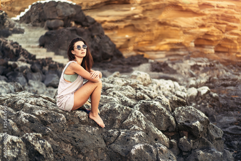 © bedya - Pretty long hair brunette tourist girl relaxing on the stones near sea.
