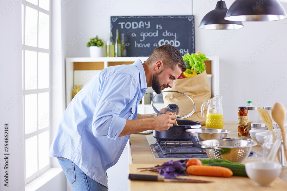 Smiling and confident chef standing in a large kitchen tasting a cooked dish Smiling and confident chef standing in a large kitchen tasting a cooked dish