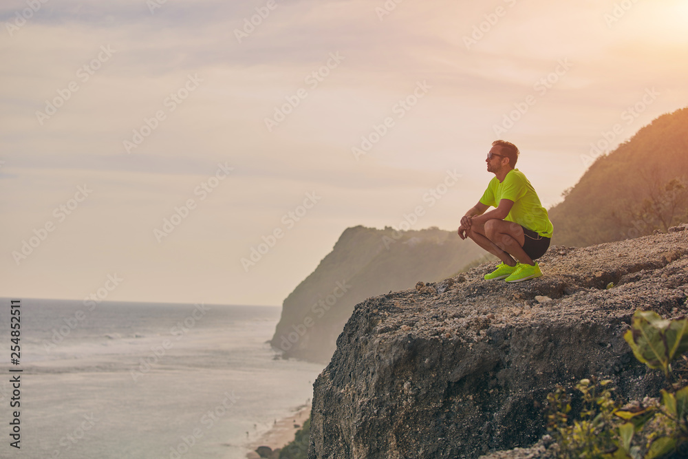 Sportsman making pause after workout on a tropical cliff. Sportsman making pause after workout on a tropical cliff.