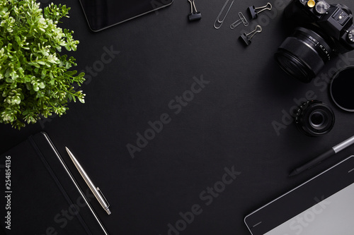 Top view of the table graphic designer with camera, lenses and diary with copy space. Flat lay shot on black background.