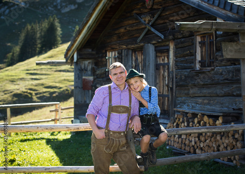 Young Bavarian family in a beautiful mountain landscape. Happy father and smiling son  in traditional Bavarian clothes   at an old hut