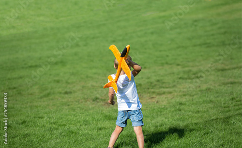 Young boy playing airplane on the meadow in summer sunny day