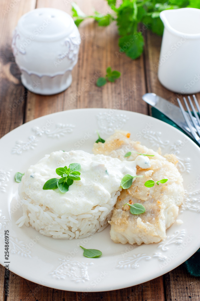 Fried cod, cooked with rice and cream sauce on a white plate, selective focus Fried cod, cooked with rice and cream sauce on a white plate, selective focus