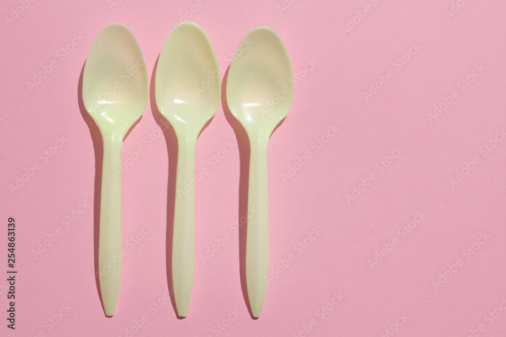 yellow plastic spoons on a pink pastel background yellow plastic spoons on a pink pastel background