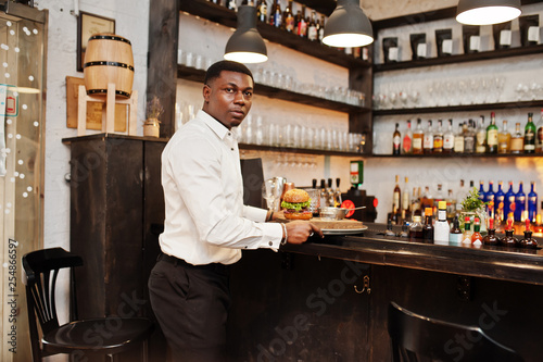 Young african american waiter man hold tray with burger at bar of restaurant. © AS Photo Family