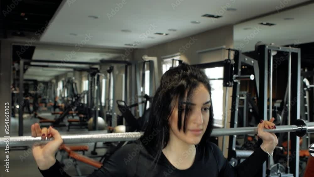 young brunette girl in black top and leggings doing exercises on the squat with a barbell. woman squat workout in gym young brunette girl in black top and leggings doing exercises on the squat with a barbell. woman squat workout in gym
