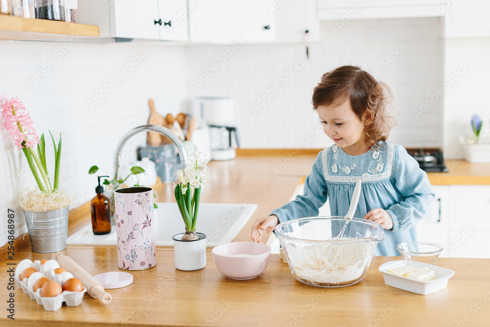 Little girl preparing easter cookies at the kitchen.