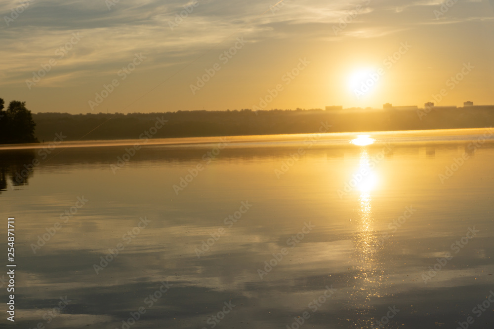 Landscape of early spring at morning sunrise on river. Bright sun lights through trees on horizon. Beautiful spring nature.