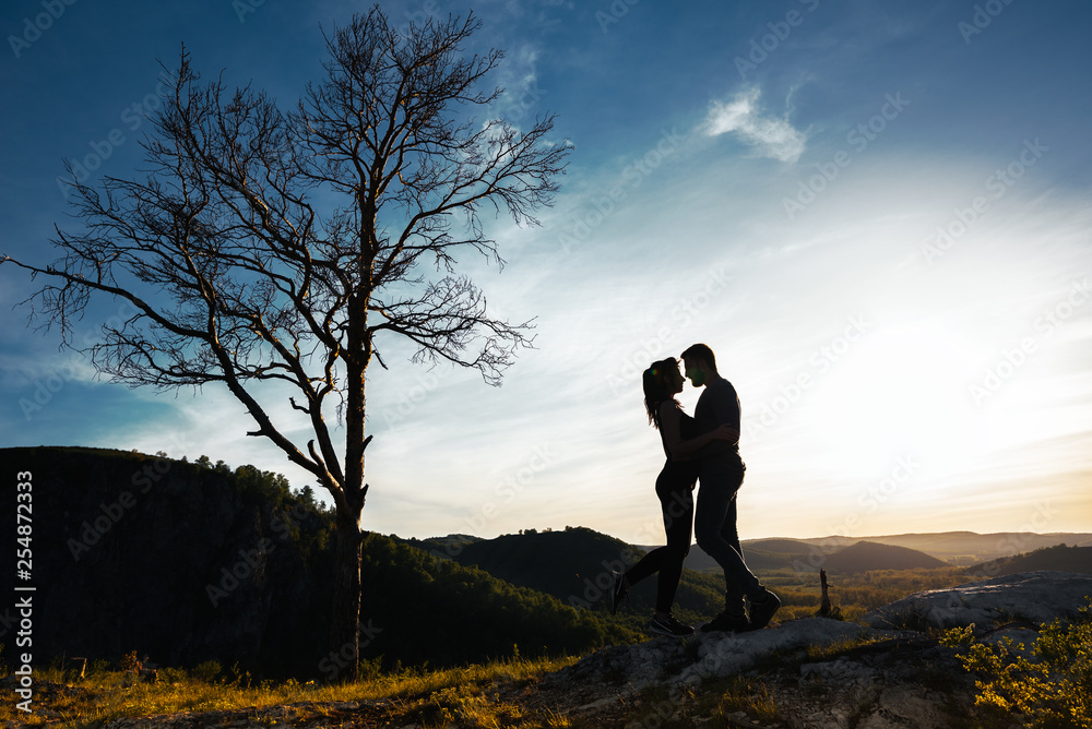 Silhouette of a couple in love. Guy and girl hugging at sunset. Couple travels. Lovers in nature. Man and woman watching the sunset. Lovers at sunset. Travel in the mountains. Honeymoon trip