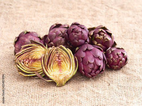 Raw artichokes, Mediterranean vegetable, uncooked on rustic hessian. One cut open to see inside.
