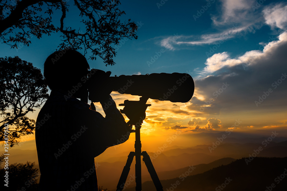 Silhouette of a landscape photographer use super telephoto lens at top of mountains during the sunset with two tone sunset sky