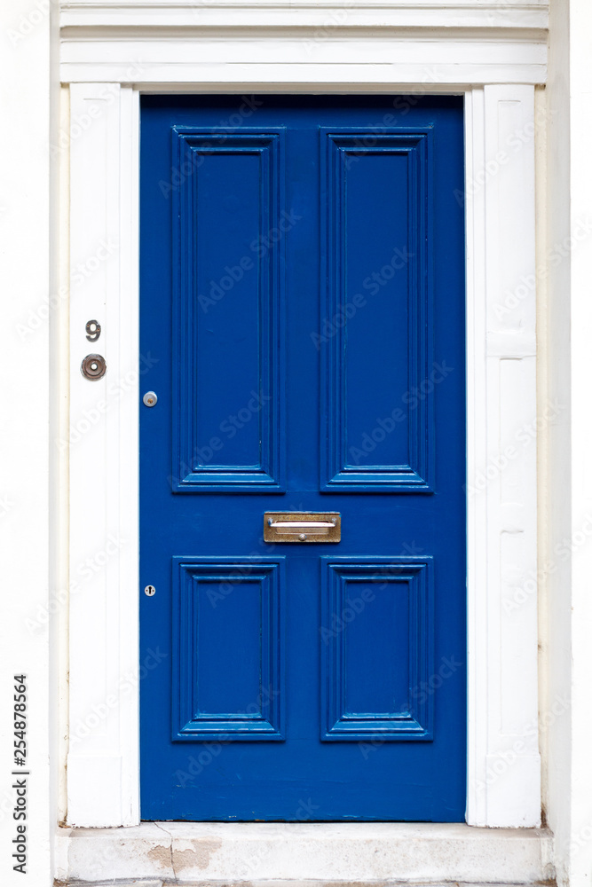 SImple and elegant old fashioned blue house door with a bronze letterbox and a white frame