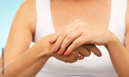 beauty and bodycare concept - close up of senior woman hands with manicure over blue background