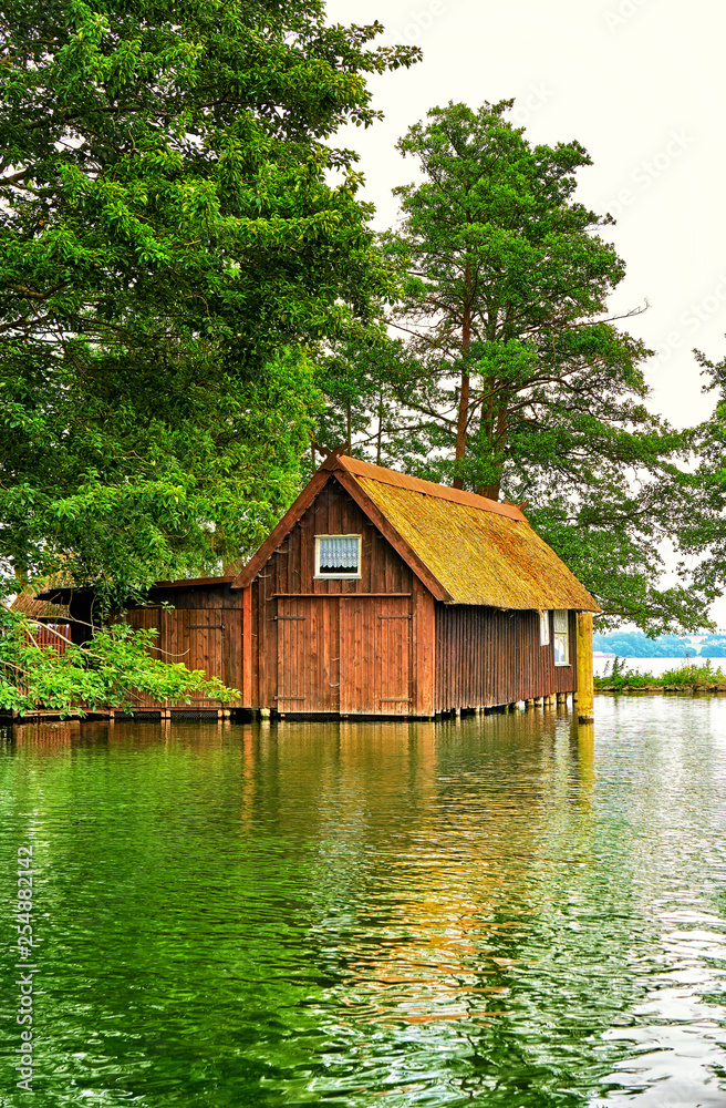 Old wooden boathouse under trees at Schwerin lake. Mecklenburg-Western Pomerania, Germany Old wooden boathouse under trees at Schwerin lake. Mecklenburg-Western Pomerania, Germany