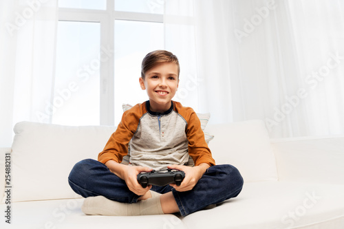gaming, technology and people concept - smiling boy with gamepad playing video game at home