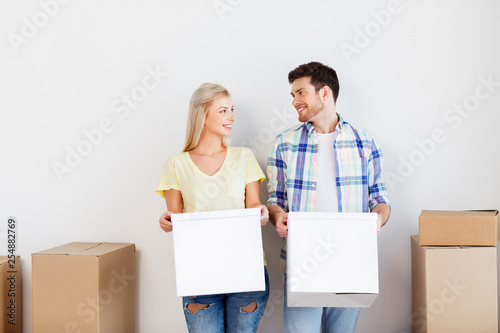 mortgage, moving, people and real estate concept - happy couple with cardboard boxes at new home