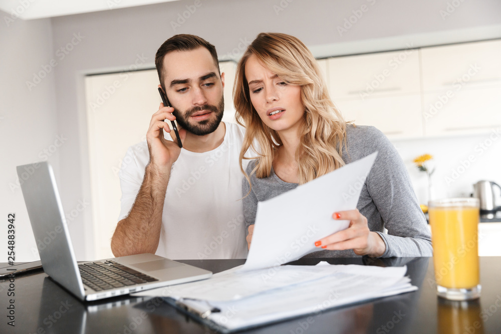 Loving couple sitting at the kitchen using laptop computer and work with documents. Loving couple sitting at the kitchen using laptop computer and work with documents.
