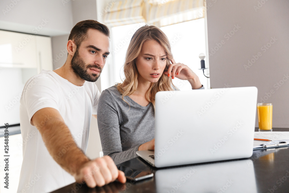 Young loving couple sitting at the kitchen using laptop computer. Young loving couple sitting at the kitchen using laptop computer.