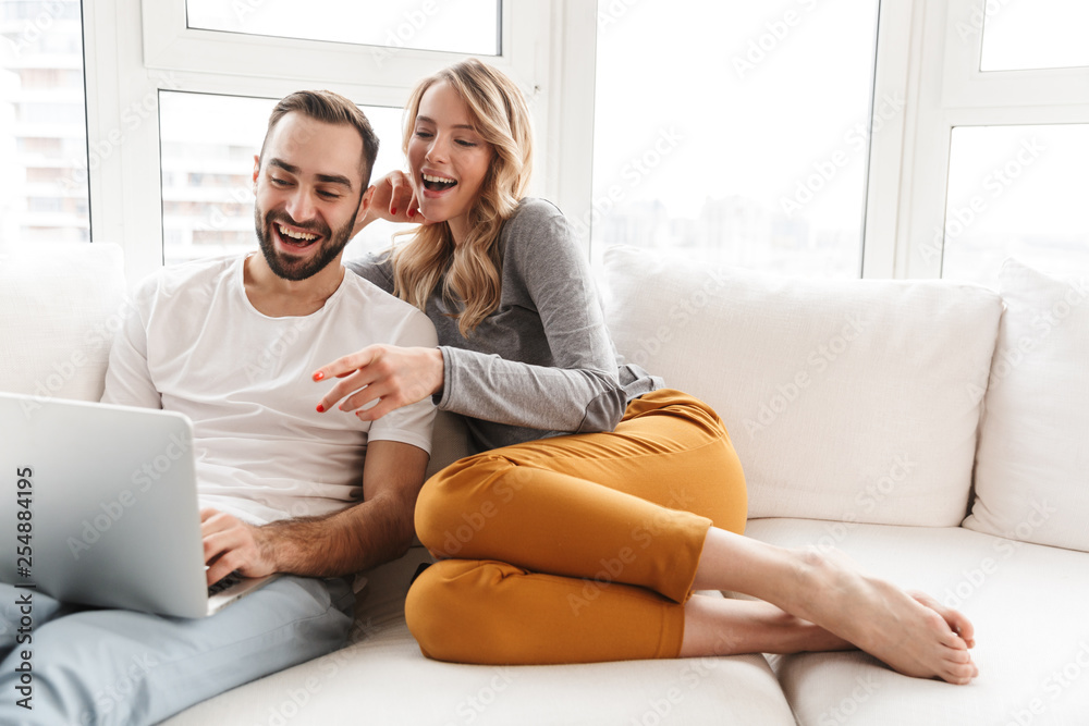 Amazing loving couple sitting indoors at home using laptop computer. Amazing loving couple sitting indoors at home using laptop computer.
