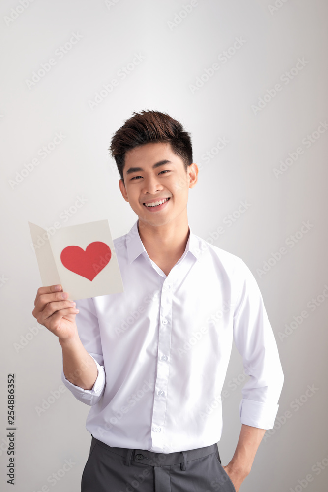 Young handsome asian man reads greeting card with heart shape on white background Young handsome asian man reads greeting card with heart shape on white background