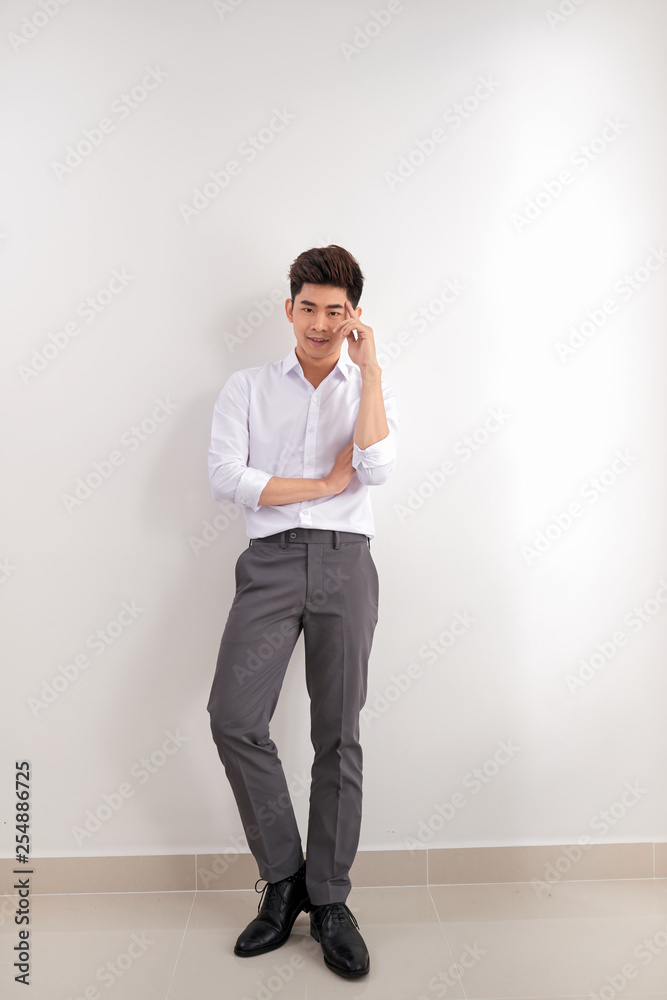 Smiling Asian man in pants and shirt standing near blank wall. Concept of businessman. Mock up Smiling Asian man in pants and shirt standing near blank wall. Concept of businessman. Mock up