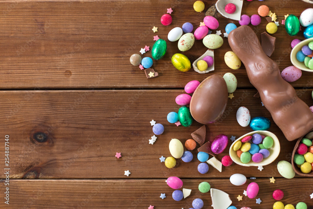 Obraz premium easter, sweets and confectionery concept - chocolate eggs, bunny and candy drops on wooden background