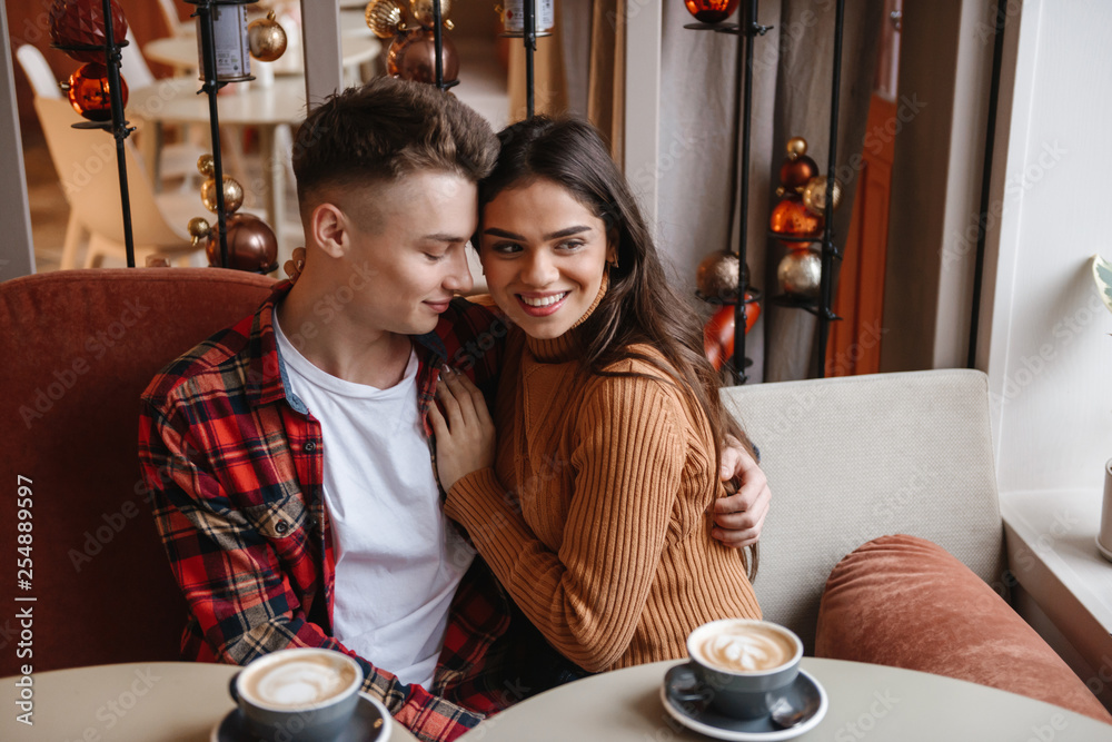 Cute young happy loving couple sitting in cafe indoors hugging.