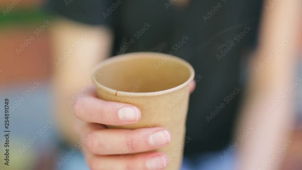 closeup woman's hand holding a paper cup with hot beverage. young woman drinks coffee outdoors and smiling. woman is holding paper cup with hot coffee. closeup woman's hand holding a paper cup with hot beverage. young woman drinks coffee outdoors and smiling. woman is holding paper cup with hot coffee.