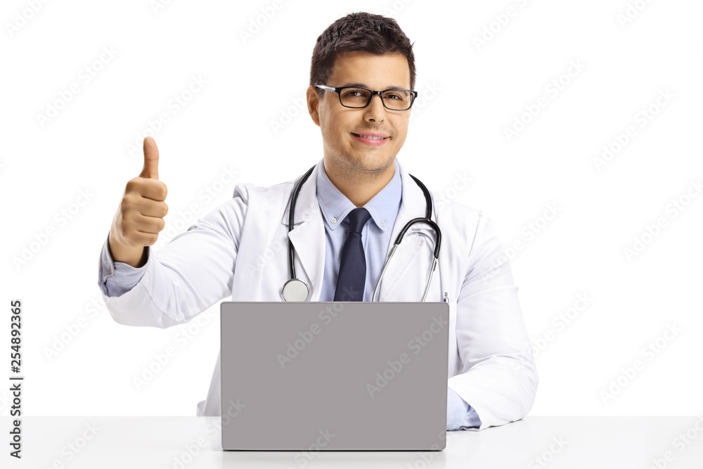 Young male doctor sitting with a laptop and showing thumbs up Young male doctor sitting with a laptop and showing thumbs up