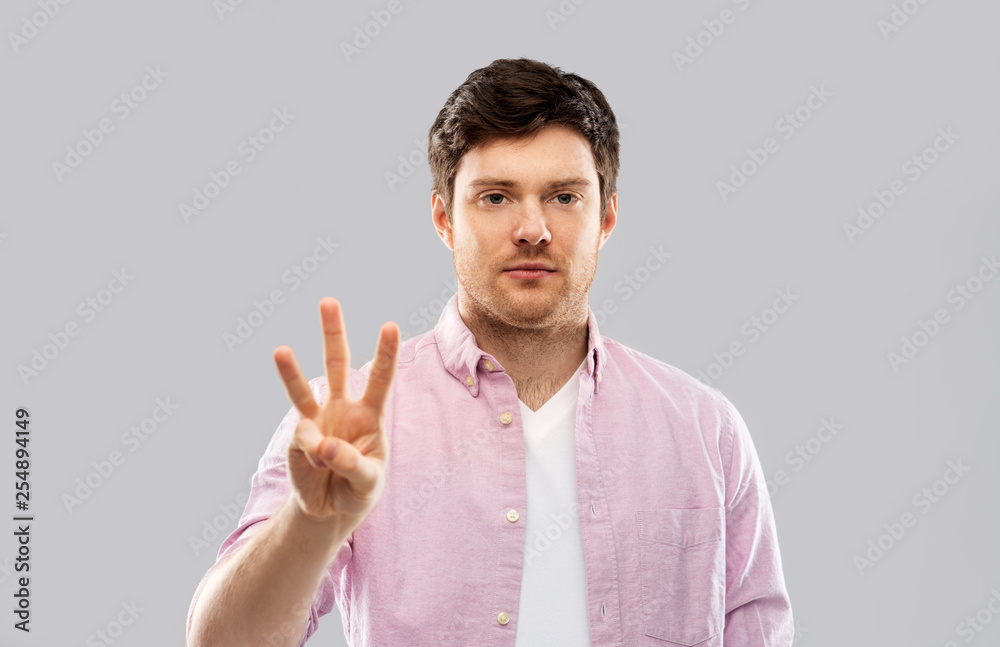count and people concept - smiling young man showing three fingers over grey background count and people concept - smiling young man showing three fingers over grey background