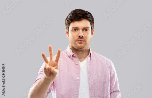 count and people concept - smiling young man showing three fingers over grey background