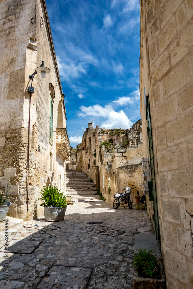 Summer day scenery street view of the amazing ancient town of the Sassi with motorbike and white puffy clouds moving on the Italian blue sky. Matera, Basilicata, Italy
