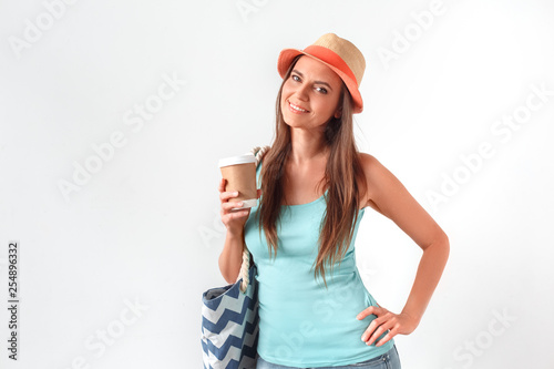 Morning refreshment. Woman in hat standing studio isolated on white with beach bag drinking cup of coffee posing to camera joyful