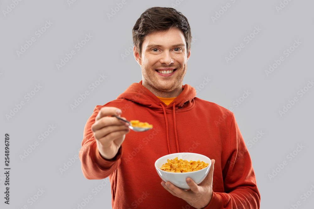 food, breakfast and people concept - smiling young man in red hoodie eating cereals over grey background food, breakfast and people concept - smiling young man in red hoodie eating cereals over grey background