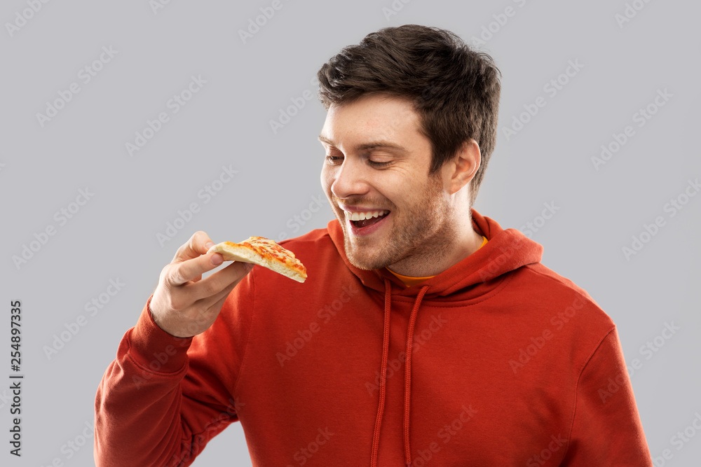 fast food and people concept - happy smiling young man in red hoodieeating pizza over grey background fast food and people concept - happy smiling young man in red hoodieeating pizza over grey background