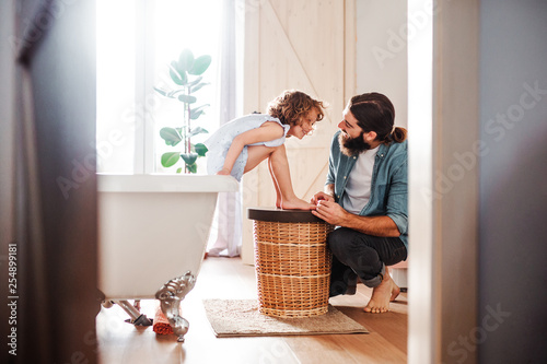 Young father painting small daugter's nails in a bathroom at home.
