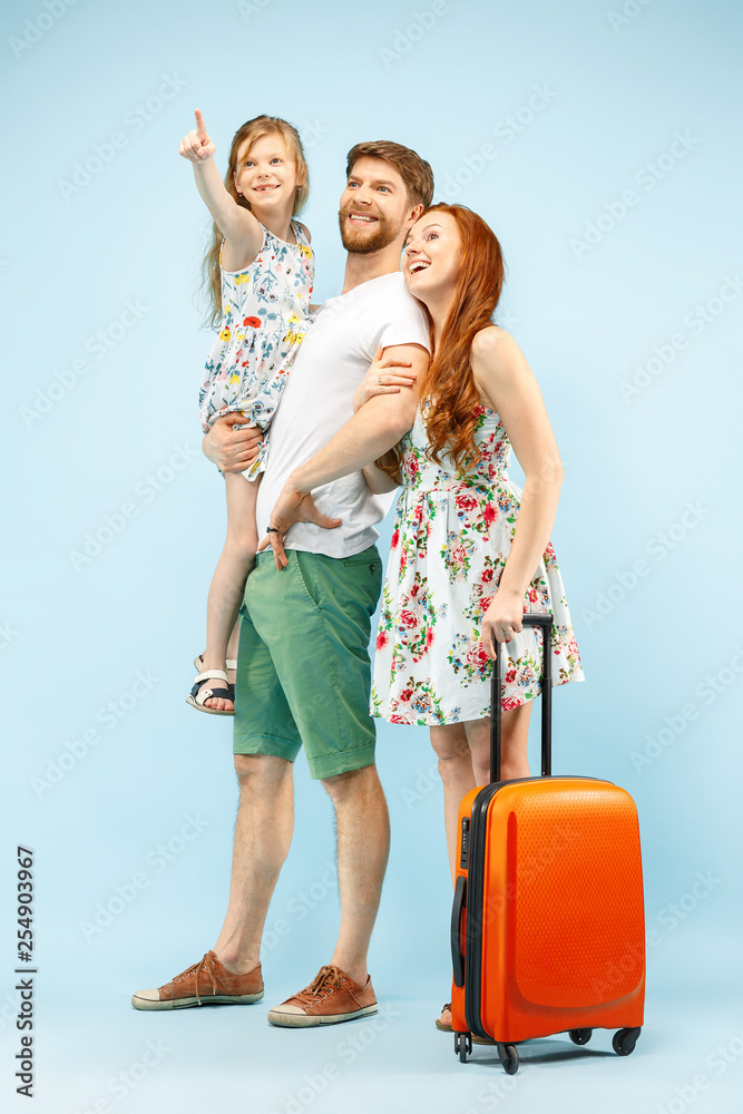 Happy surprised parent with daughter and suitcase at studio isolated on blue background. Travel, vacation, parenthood, togetherness, tourism concept. Happy surprised parent with daughter and suitcase at studio isolated on blue background. Travel, vacation, parenthood, togetherness, tourism concept.