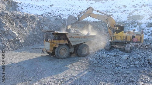 Huge career dump truck working in a career.  An excavator in a quarry loads a dump truck with rock, soil, stones.