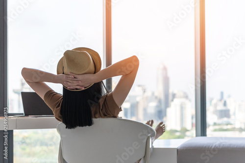 Life quality concept with young woman relaxing and resting in comfortbusiness hotel guest room or luxury home living room looking toward beautiful city view of cityscape photo