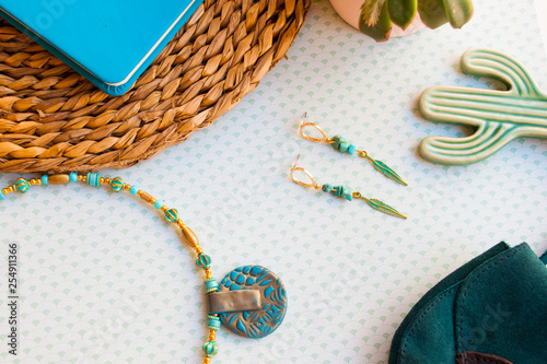 Fashion flat lay with turquoise gold earrings and choker, small bag, notebook and green flower.