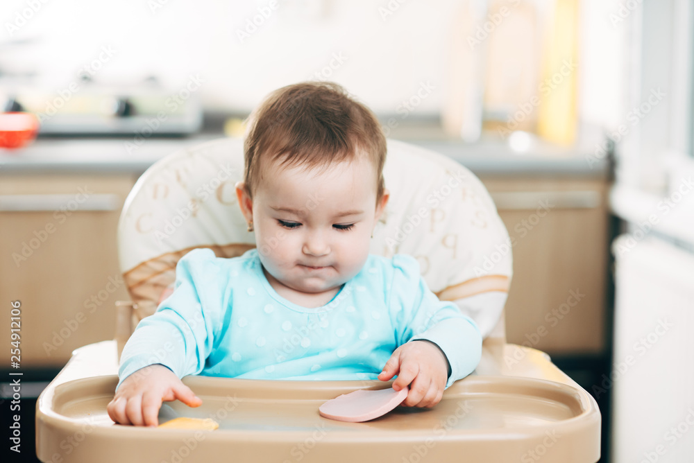 a little girl in a high chair with a piece of boiled sausage in her hands a little girl in a high chair with a piece of boiled sausage in her hands
