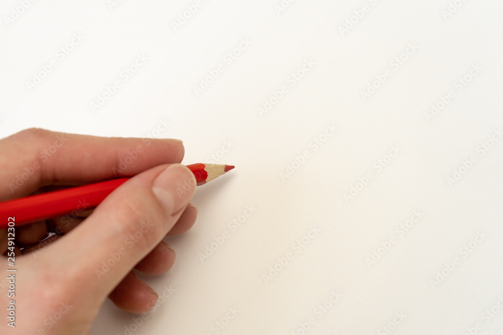 Hand with red pencil writing note on white paper on the left Hand with red pencil writing note on white paper on the left