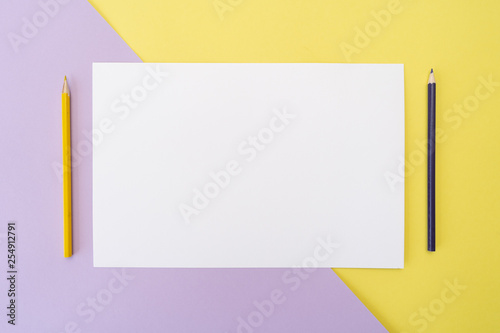 Yellow and purple pencils and white piece of paper on yellow and purple background. Art, scool or office shoot