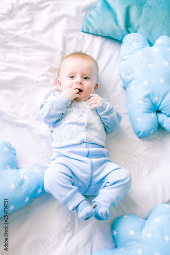 Cute toddler boy on bed at home surrounded by blue pillows