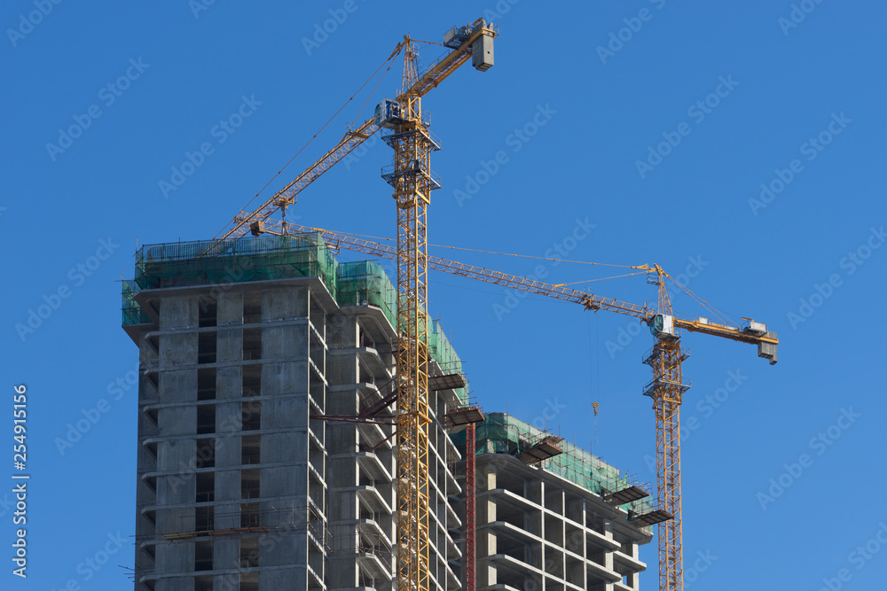 Urban landscape with views of the house under construction and cranes against the blue sky. Urban landscape with views of the house under construction and cranes against the blue sky.