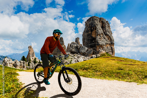 Tourist cycling in Cortina d'Ampezzo, stunning Cinque Torri and Tofana in background. Man riding MTB enduro flow trail. South Tyrol province of Italy, Dolomites.