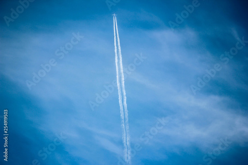 Contrail cloud appears as an aircraft drifts across the clear blue sky,