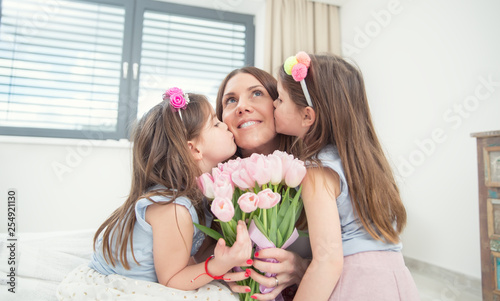 Happy mother's day concept. Little daughters twins kiss their mother with a tulip bouquet