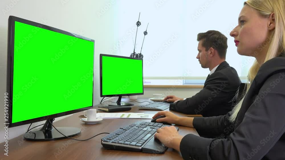 Two office workers, man and woman, work on computers with green screens