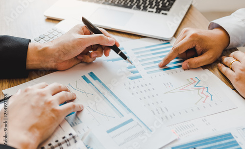 Two businessmen are pointing to the company sales graph paper and then analyzing together.